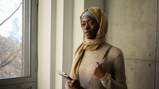 Black woman in hijab with notebooks near window